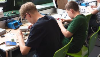 Zu sehen sind zwei Jungen, die nebeneinander sitzen und ihren Bausatz zusammenbauen und löten.