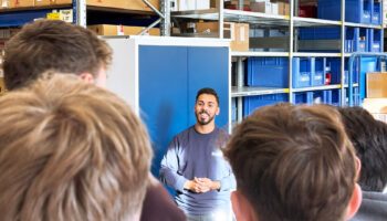 Zu sehen ist ein Mitarbeiter aus dem Lager, der den Schülerinnen und Schüler gerade mehr über seinen Beruf erzählt