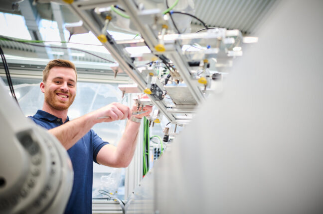 Ein Sonplas-Mitarbeiter steht links neben einer Sondermaschine und montiert dort ein Bauteil. Er lächelt in die Kamera.