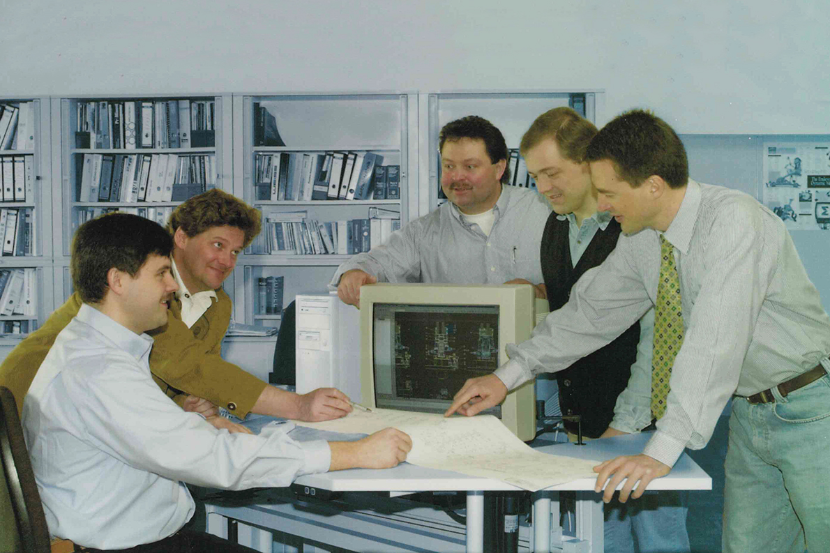 Die fünf Gründer von Sonplas haben sich auf dem historischen Originalfoto um einen PC und Konstruktionszeichnungen auf Papier versammelt.