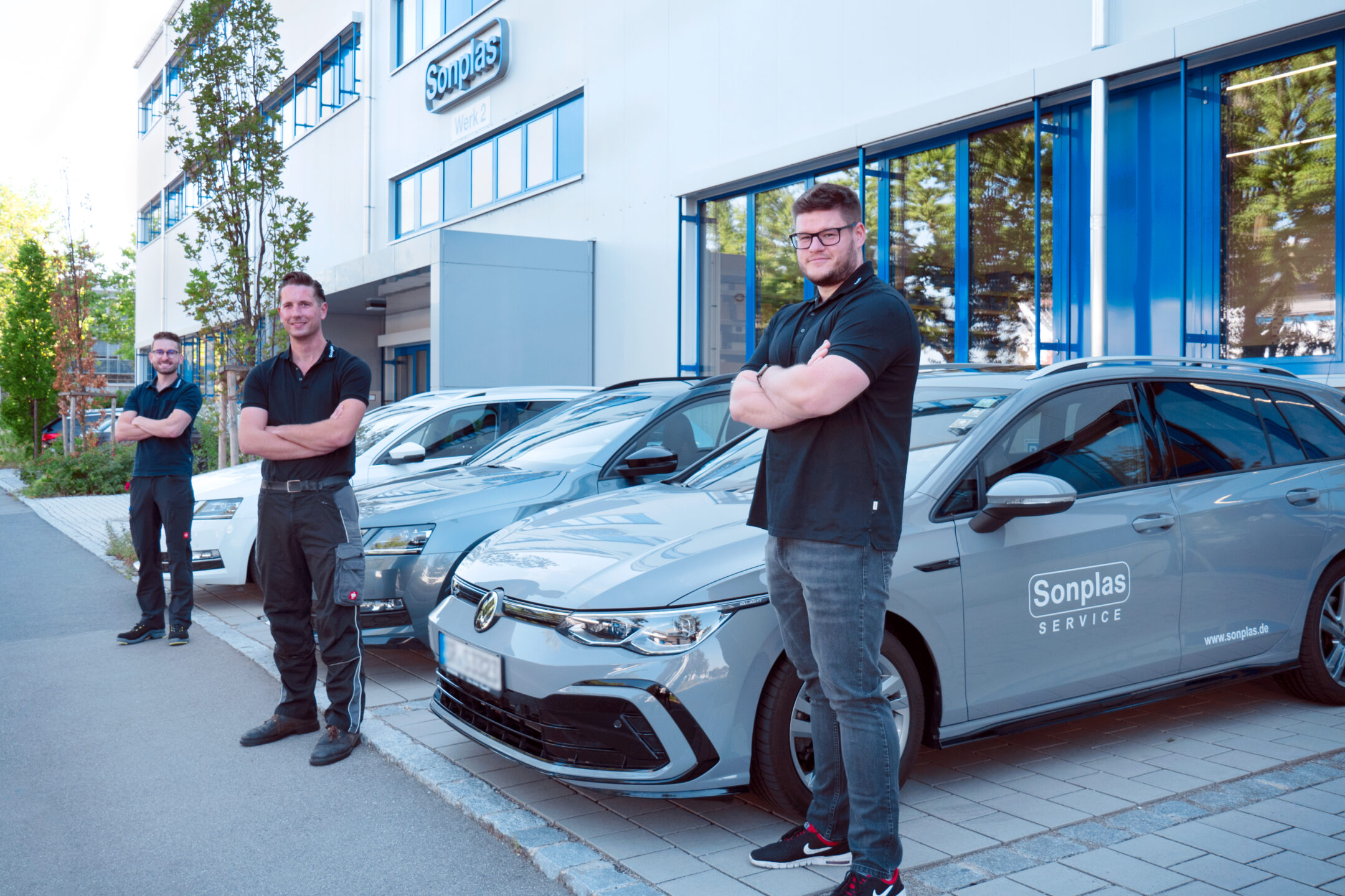 Drei Sonplas Mitarbeiter stehen mit verschränkten Armen vor drei Service Autos von Sonplas vor dem Werk