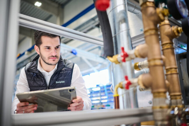 Sonplas Mitarbeiter steht vor einer Anlage, schaut diese an und hat dabei ein Tablet in der Hand